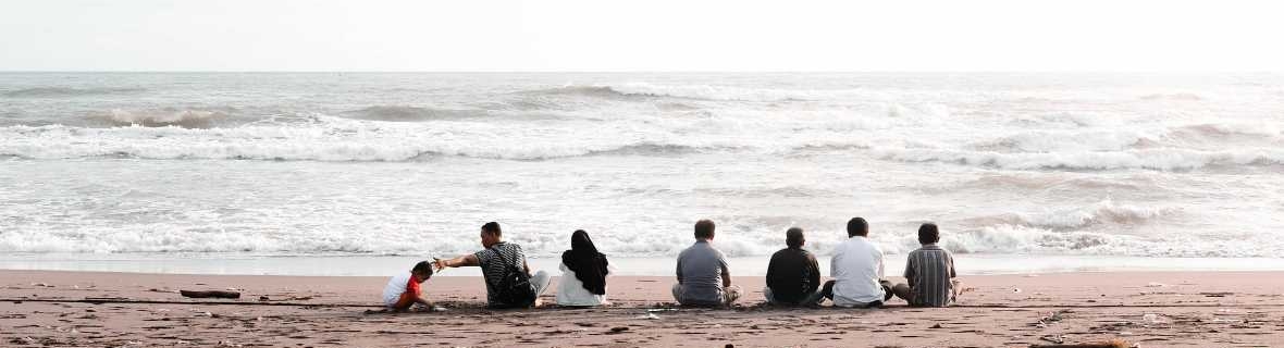 Group of people sitting on beach with backs to camera