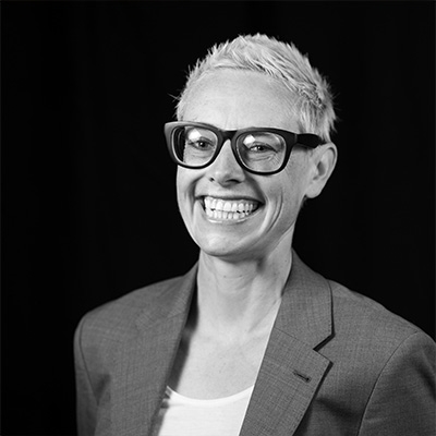 Anna Zivarts | An Island Press author | A black-and-white portrait of a White woman smiling with short blond hair and thick black glasses